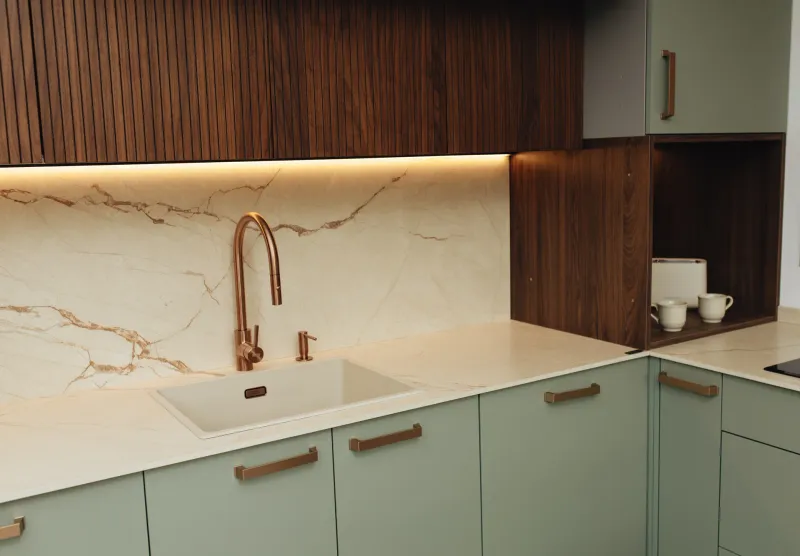 Cocina moderna con frentes verdes, armarios de madera y grifo de cobre