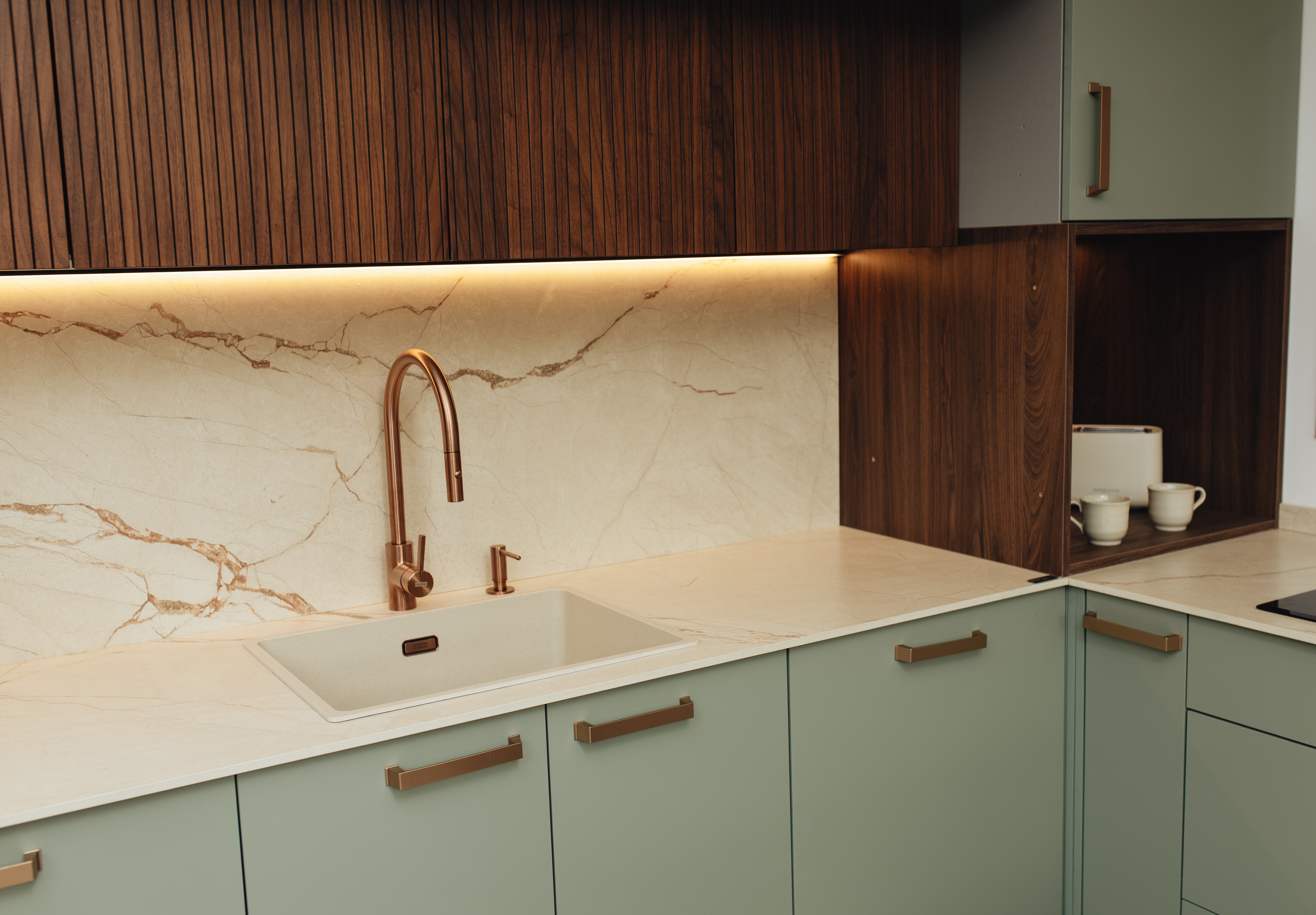 Cocina moderna con frentes verdes, armarios de madera y grifo de cobre