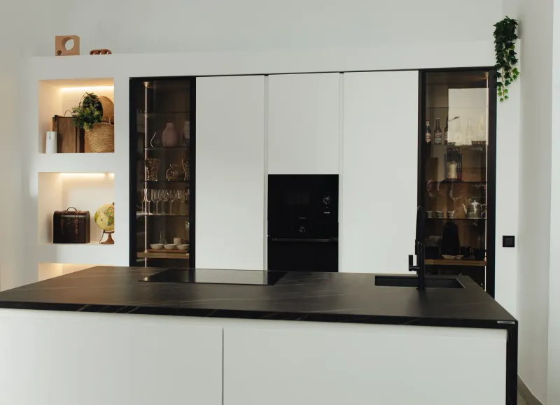 Cocina moderna con frentes blancos, isla de mármol negro y vitrinas de cristal