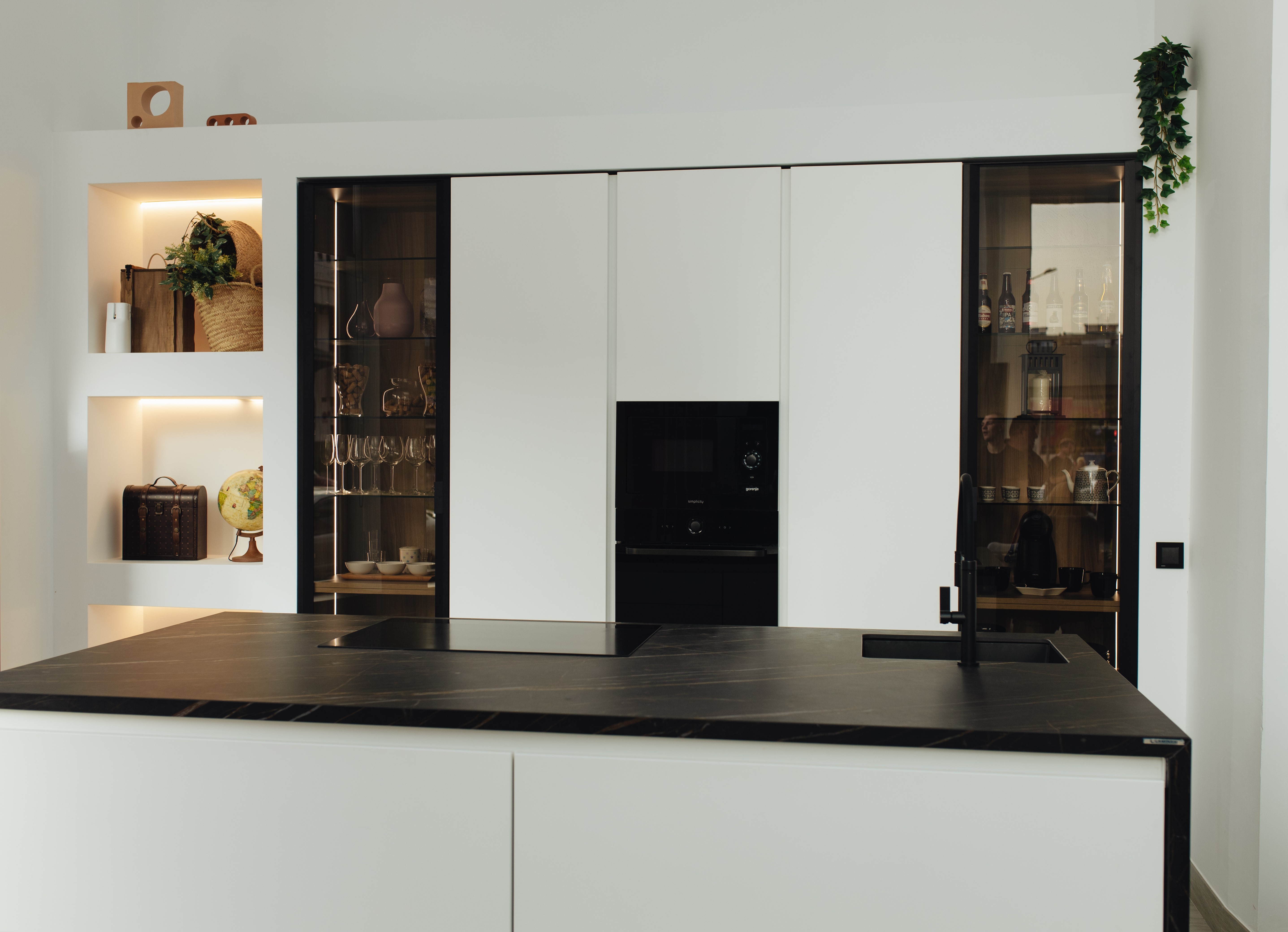 Cocina moderna con frentes blancos, isla de mármol negro y vitrinas de cristal